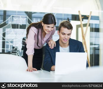 Young businessman and businesswoman using laptop at table in office