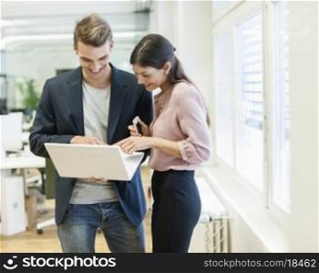 Young businessman and businesswoman using laptop in office
