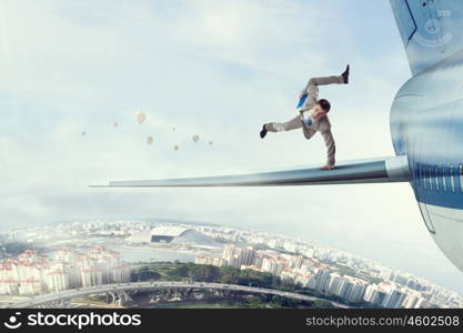 Young businessman breakdancer. Active businessman making handstand on airplane wing