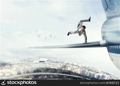 Young businessman breakdancer. Active businessman making handstand on airplane wing
