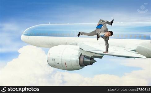 Young businessman breakdancer. Active businessman making handstand on airplane wing