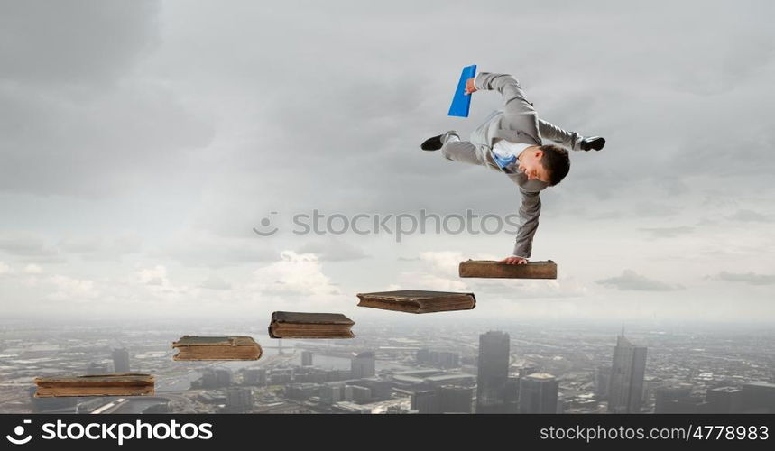 Young businessman breakdancer. Active businessman making handstand on pile of books