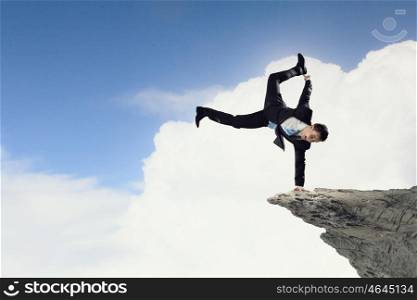 Young businessman breakdancer. Active businessman making handstand on rock edge