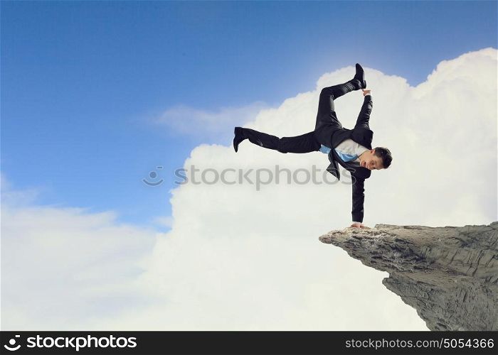 Young businessman breakdancer. Active businessman making handstand on rock edge