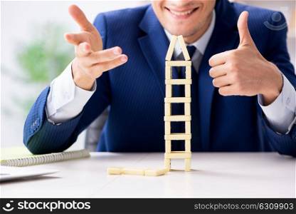 Young businessman building domino tower in office