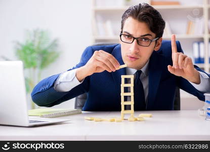 Young businessman building domino tower in office