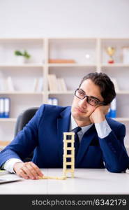 Young businessman building domino tower in office