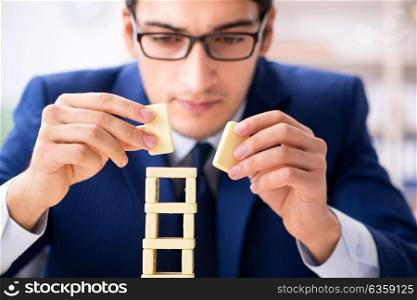 Young businessman building domino tower in office