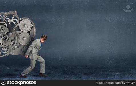Young businessman carrying huge gears mechanism on back. Making mechanism work