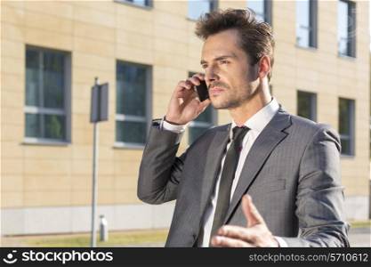 Young businessman conversing on cell phone against office building