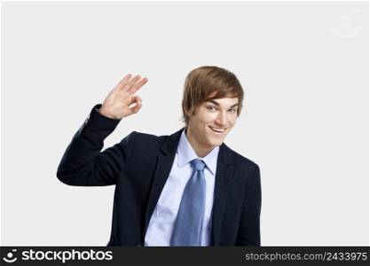 Young businessman doing a Okay signal to the camera, over a gray background