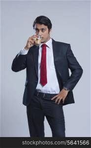 Young businessman drinking tea against gray background