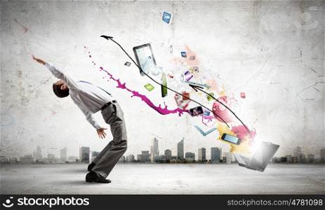 Young businessman evading colorful splashes flying from laptop. Impressive technology innovations