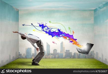 Young businessman evading colorful splashes flying from laptop. Impressive technology innovations