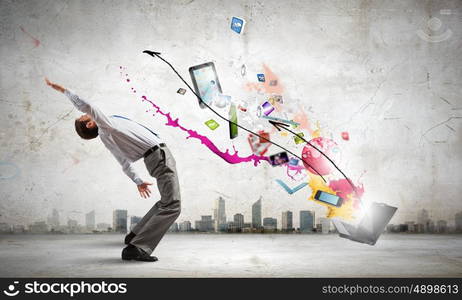 Young businessman evading colorful splashes flying from laptop. Impressive technology innovations