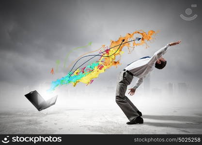 Young businessman evading colorful splashes flying from laptop. Impressive technology innovations