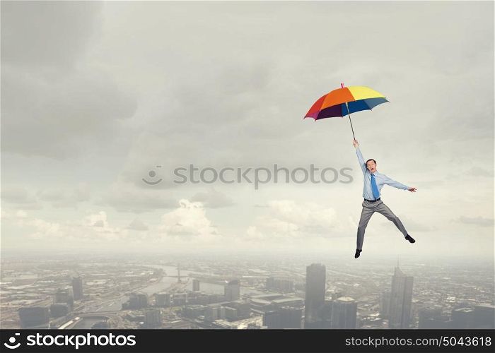 Young businessman flying high in sky on umbrella. Man fly on umbrella