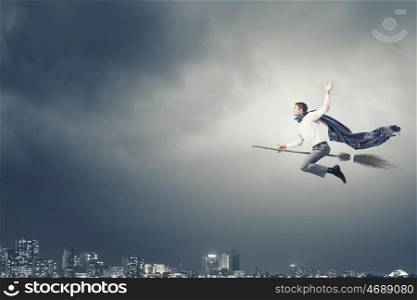 Young businessman flying on broom high in sky. Businessman on broom