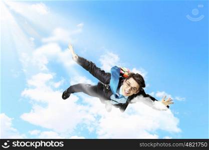 Young businessman flying with parachute on back. Conceptual image of young businessman flying with parachute on back