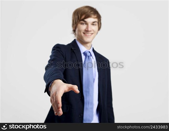 Young businessman giving a hand shake, over a gray background