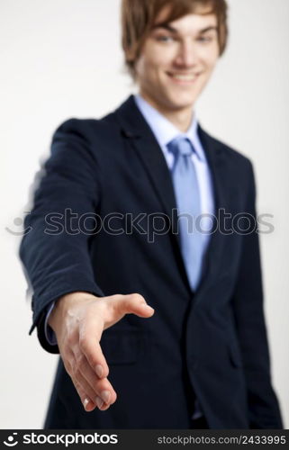 Young businessman giving a hand shake, over a gray background