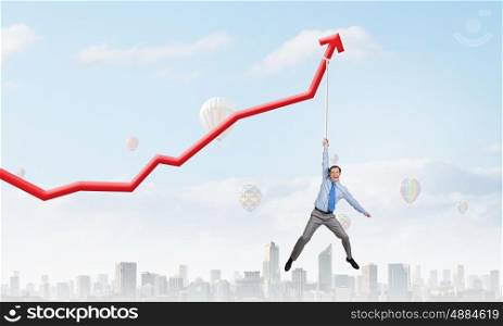 Young businessman hanging on increasing red graph. Growing graph