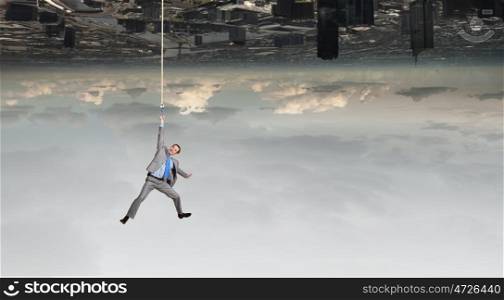Young businessman hanging on rope above city. Man hang on rope