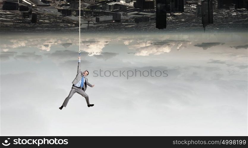 Young businessman hanging on rope above city. Man hang on rope