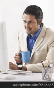 Young businessman having coffee while using computer in office