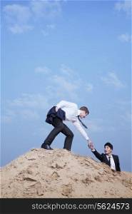 Young businessman helping another businessman get to the top of the hill in the desert