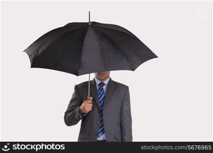 Young businessman hiding under umbrella against gray background