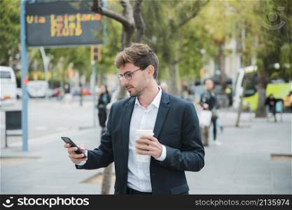 young businessman holding disposable coffee cup looking mobile phone