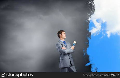 Young businessman holding paint brush and paintings on wall