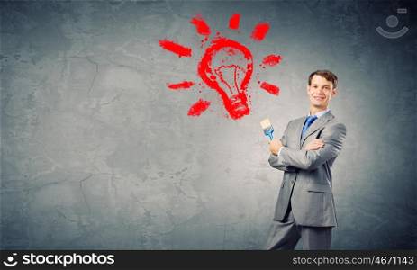 Young businessman holding paint brush and paintings on wall
