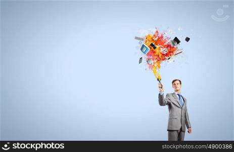 Young businessman holding paint brush with colorful splashes
