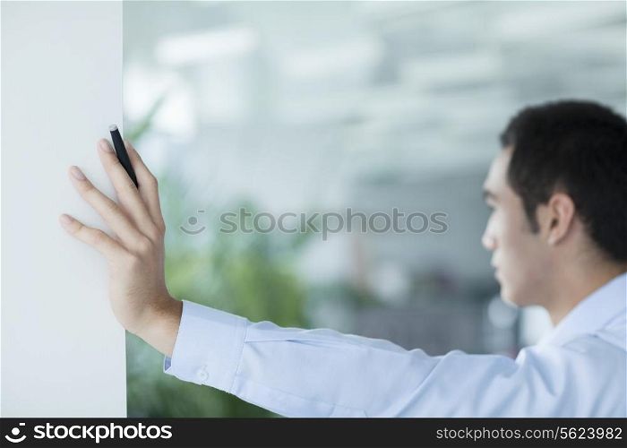 Young businessman holding pen and leaning on doorway in the office