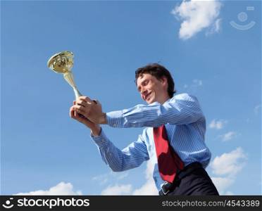 young businessman in a suit with a golden cup against blue sky