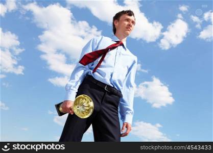 young businessman in a suit with a golden cup against blue sky