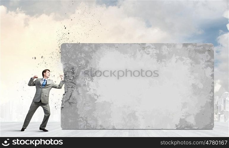 Young businessman in anger crashing cement wall. No barriers on my way