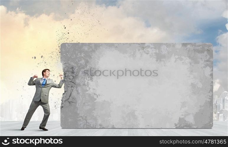 Young businessman in anger crashing cement wall. No barriers on my way