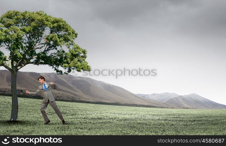 Young businessman in anger fighting with green tree. Furious businessman