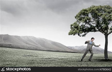 Young businessman in anger fighting with green tree. Furious businessman