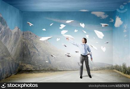 Young businessman in concrete room with paper plane in hand