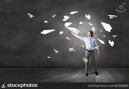 Young businessman in concrete room with paper plane in hand