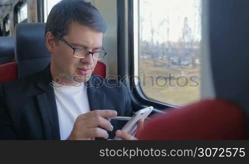 Young businessman in glasses traveling by train. He using pen to browse the internet during the trip. He is thoughtful and looking out the window