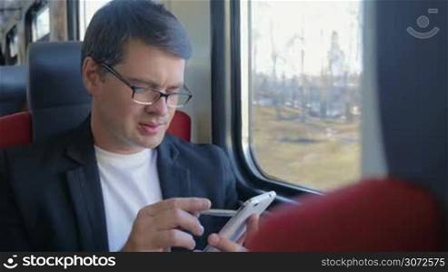 Young businessman in glasses traveling by train. He using pen to browse the internet during the trip. He is thoughtful and looking out the window