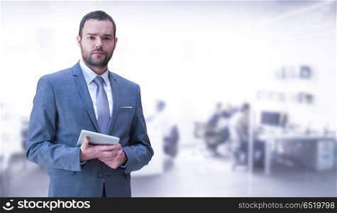 Young businessman in his office. Portrait of young junior businessman using tablet in front of his big modern office