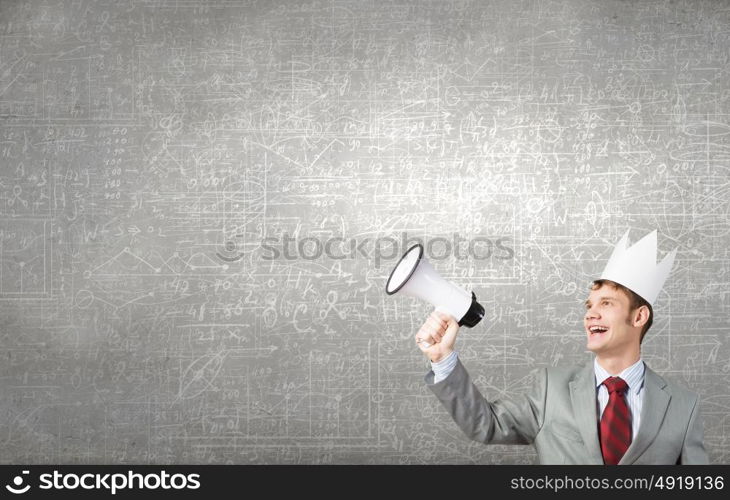 Young businessman in paper crown screaming in megaphone. Listen everyone