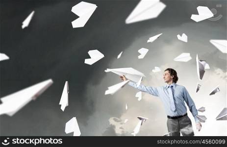 Young businessman in pile of books with paper plane in hand