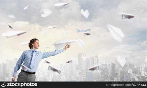 Young businessman in pile of books with paper plane in hand